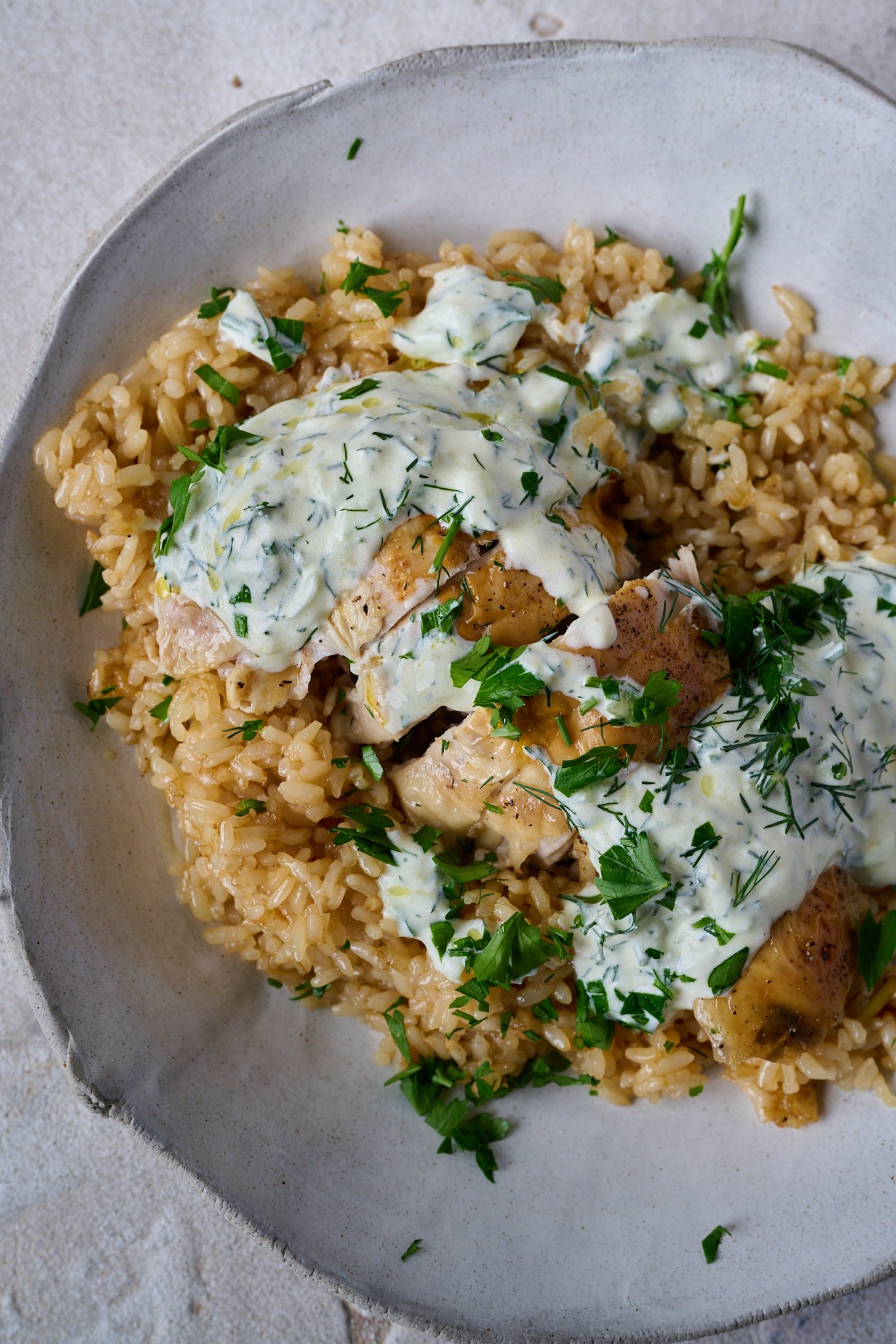 One pan chicken and garlic rice is in a bowl. Chicken is sliced and is sitting on a bed of rice with yoghurt sauce and herbs sprinkled all over.