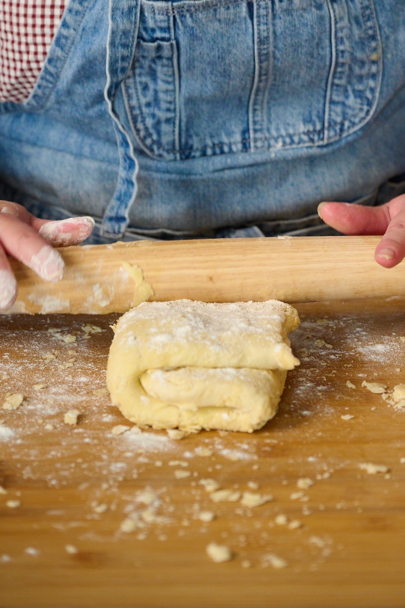 folded puff pastry is being rolled out with rolling pin.