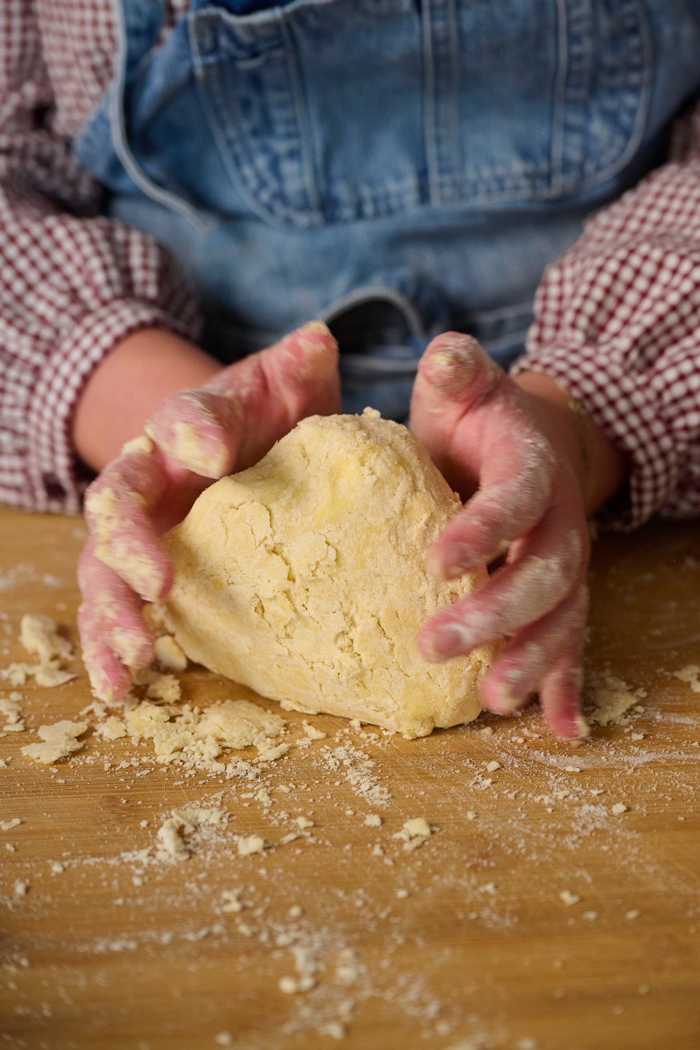 Ball of puff pastry is on wooden chopping board with hands around it.