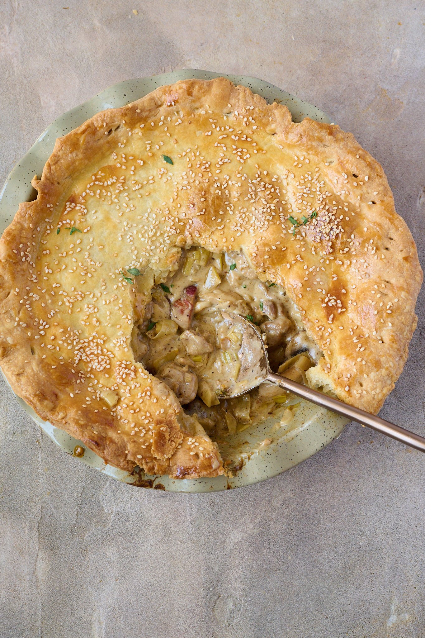 Creamy Chicken, Mushroom & Bacon Pot Pie is in green pie dish with a slice taken out of the middle and gold spoon sitting out of side. 