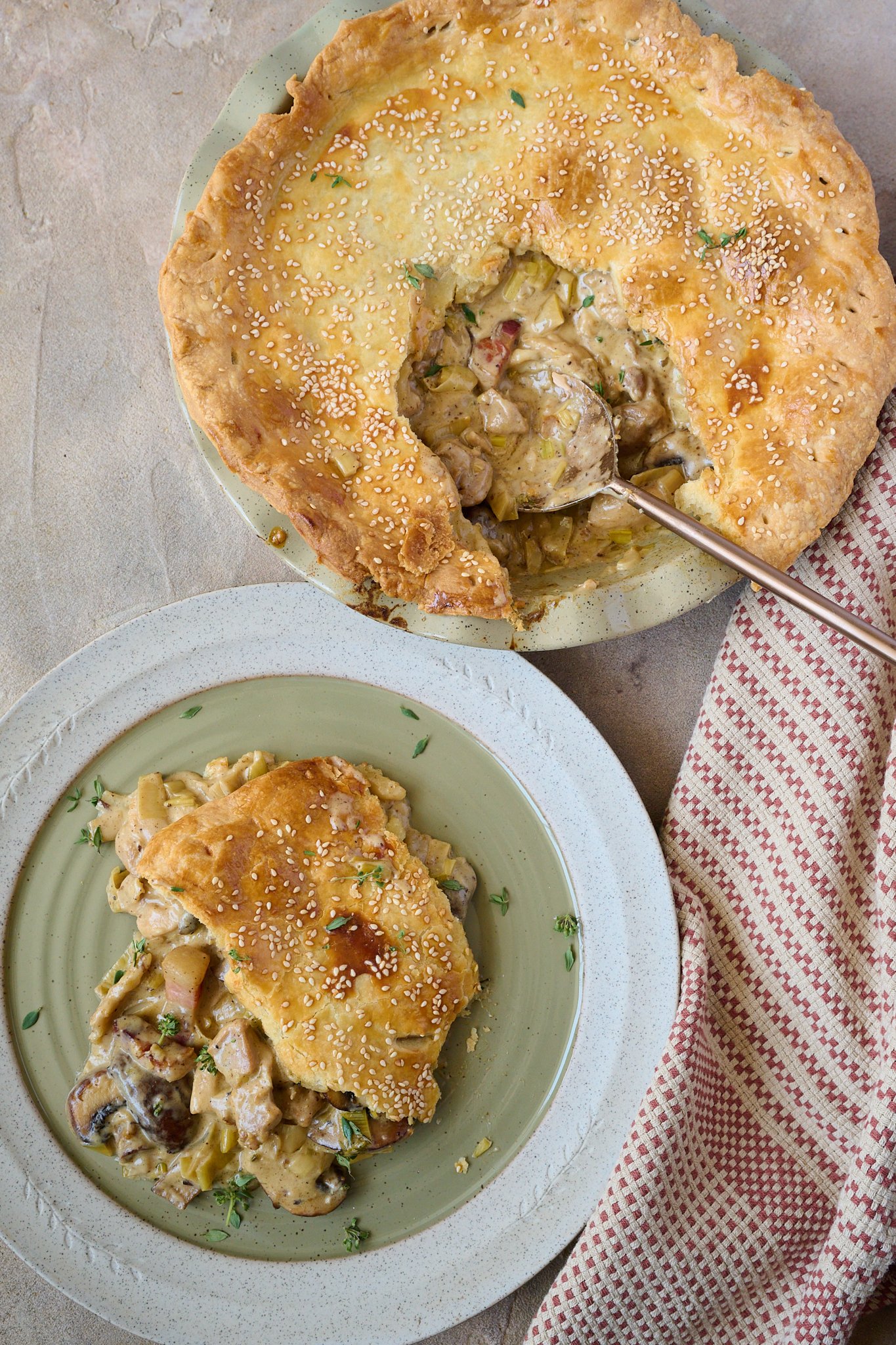 Creamy Chicken, Mushroom & Bacon Pot Pie is in green pie dish with a slice taken out of the middle and gold spoon sitting out of side. There is a green plate to the side of the pie with a slice of the pie on it.
