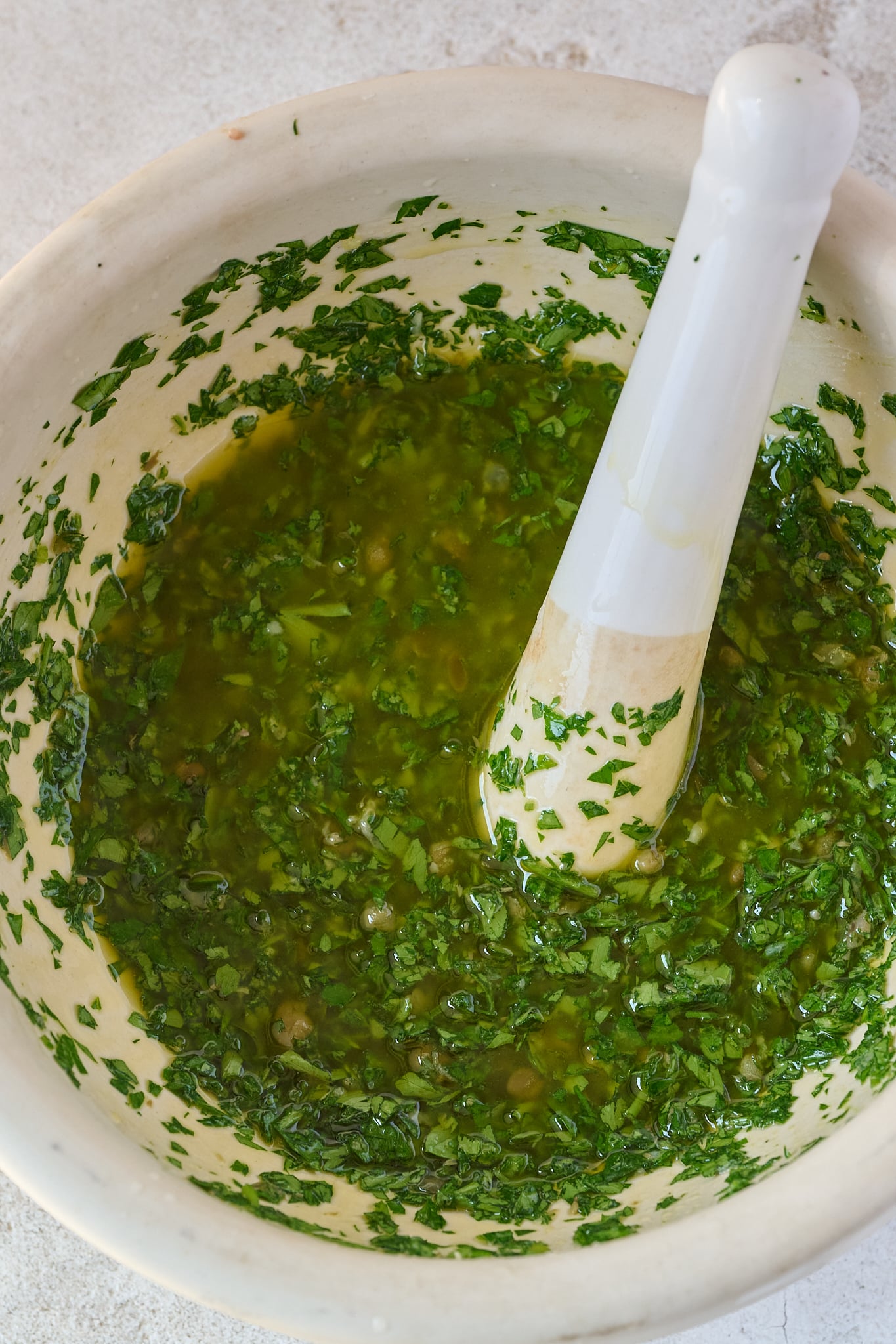 White mortar and pestle has salsa verde inside it.