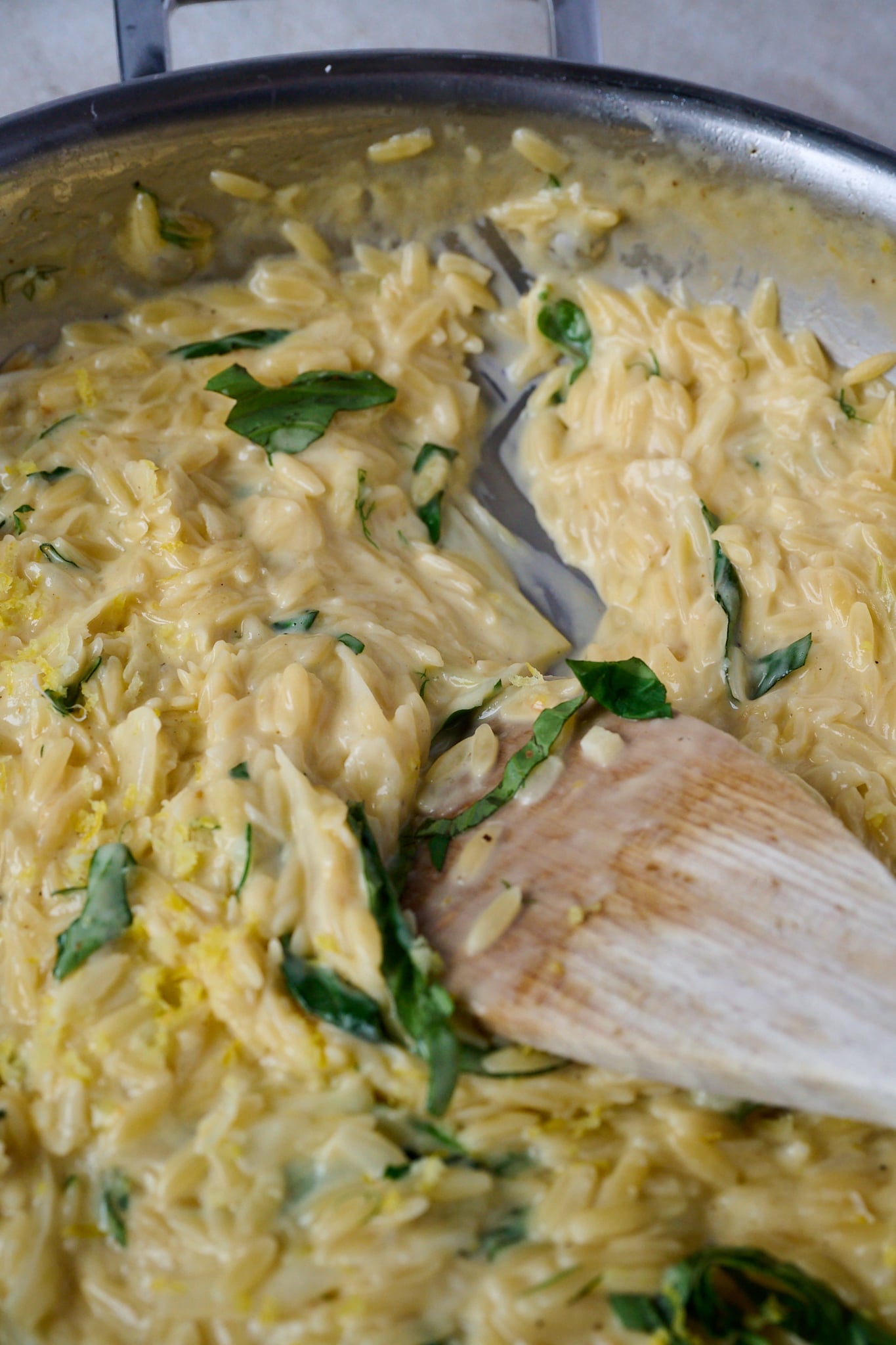 Caramelized Fennel One Pot Orzo Pasta is cooked and in large stainless steel pan with a wooden spoon sticking out of the pan.