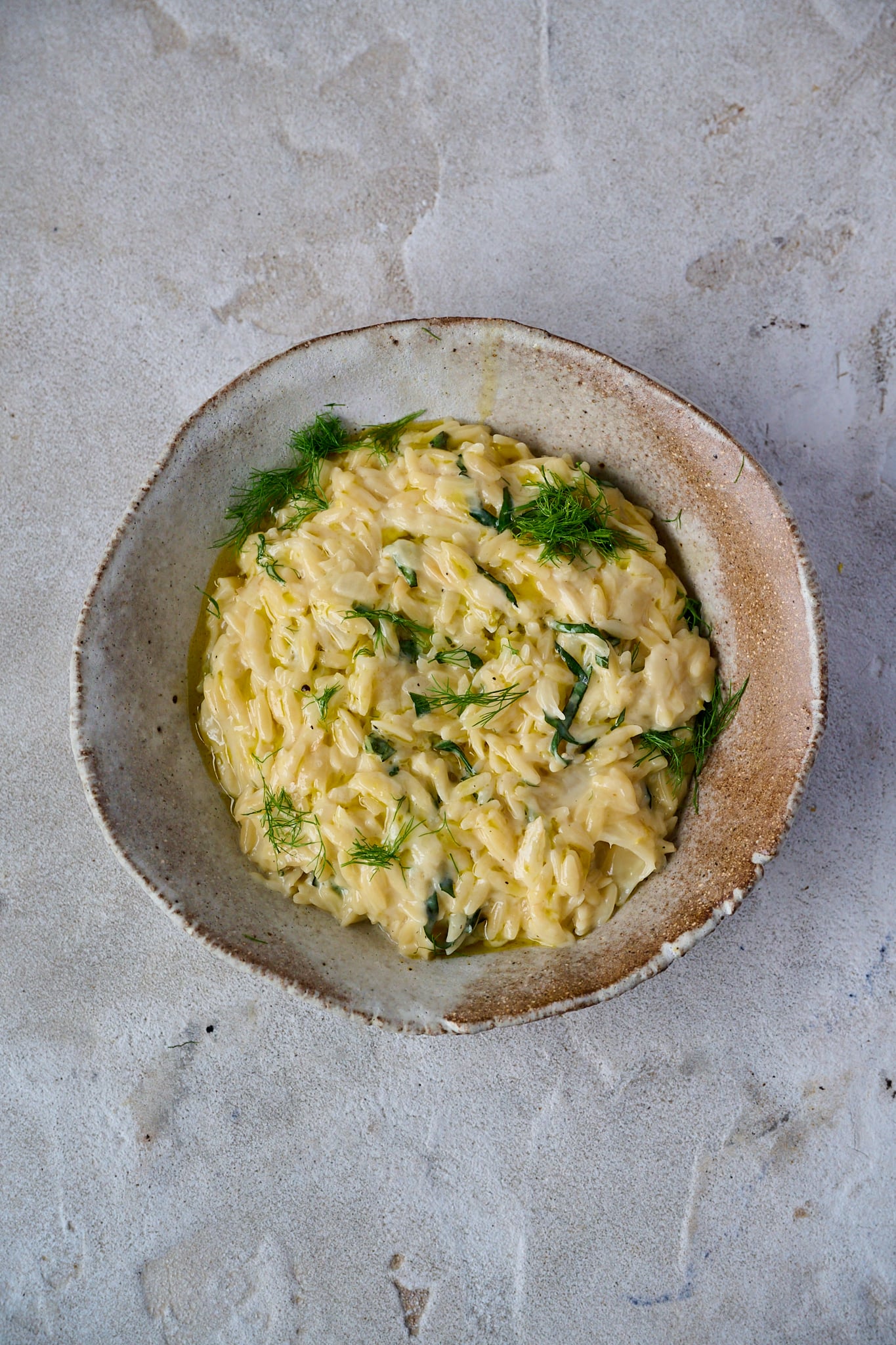 Caramelized Fennel One Pot Orzo Pasta is in brown round bowl with fresh basil and fennel fronds sprinkled all over.