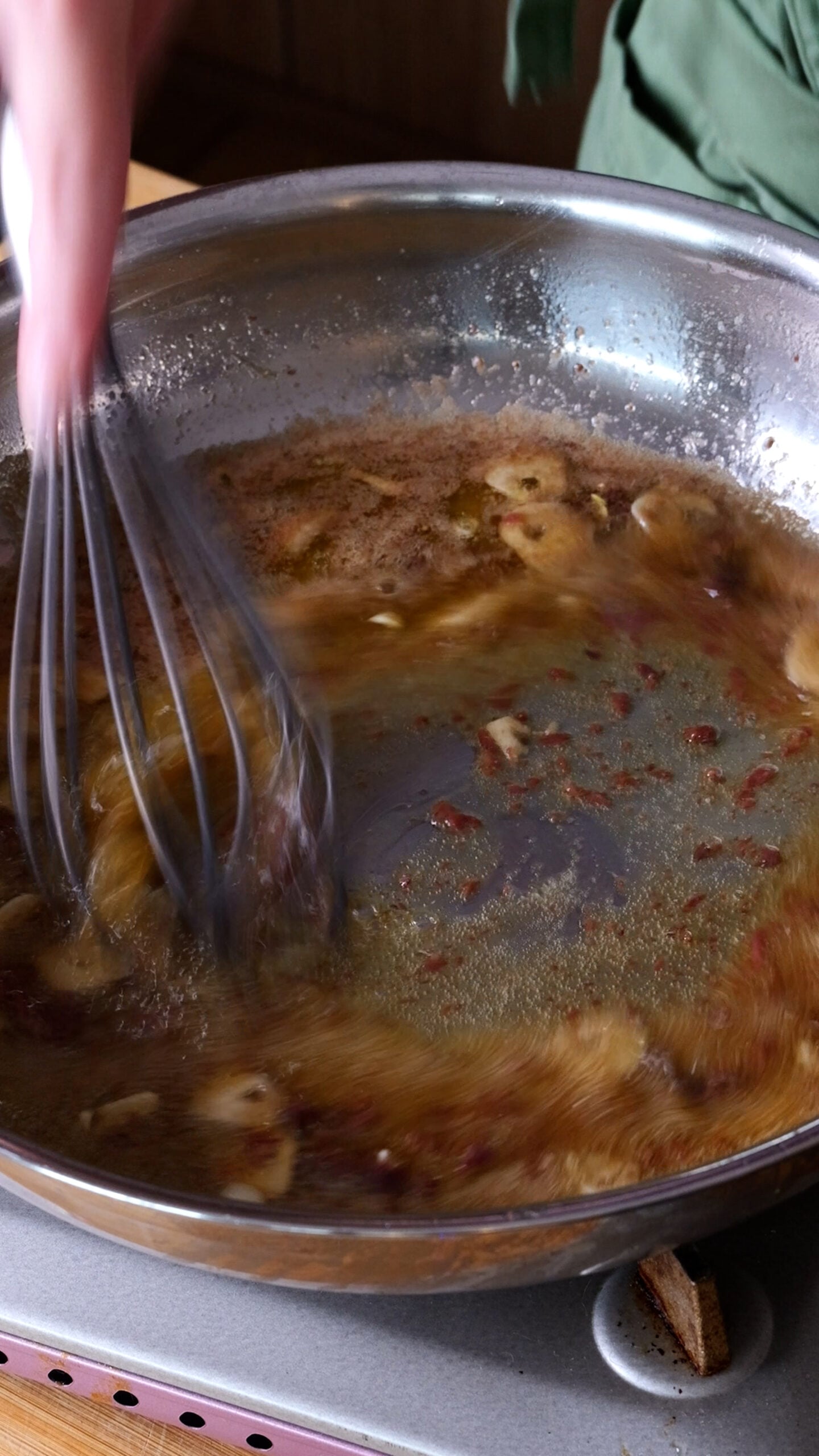 Whisk is going through anchovy butter sauce is large stainless steel pan