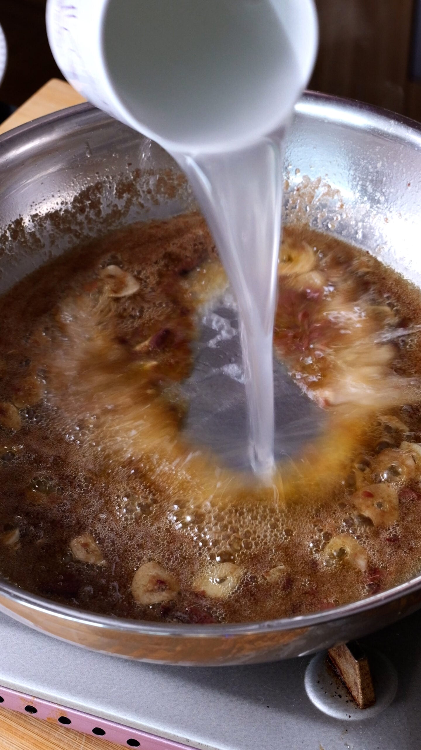 Pasta water being added to sauce in large stainless steel pan