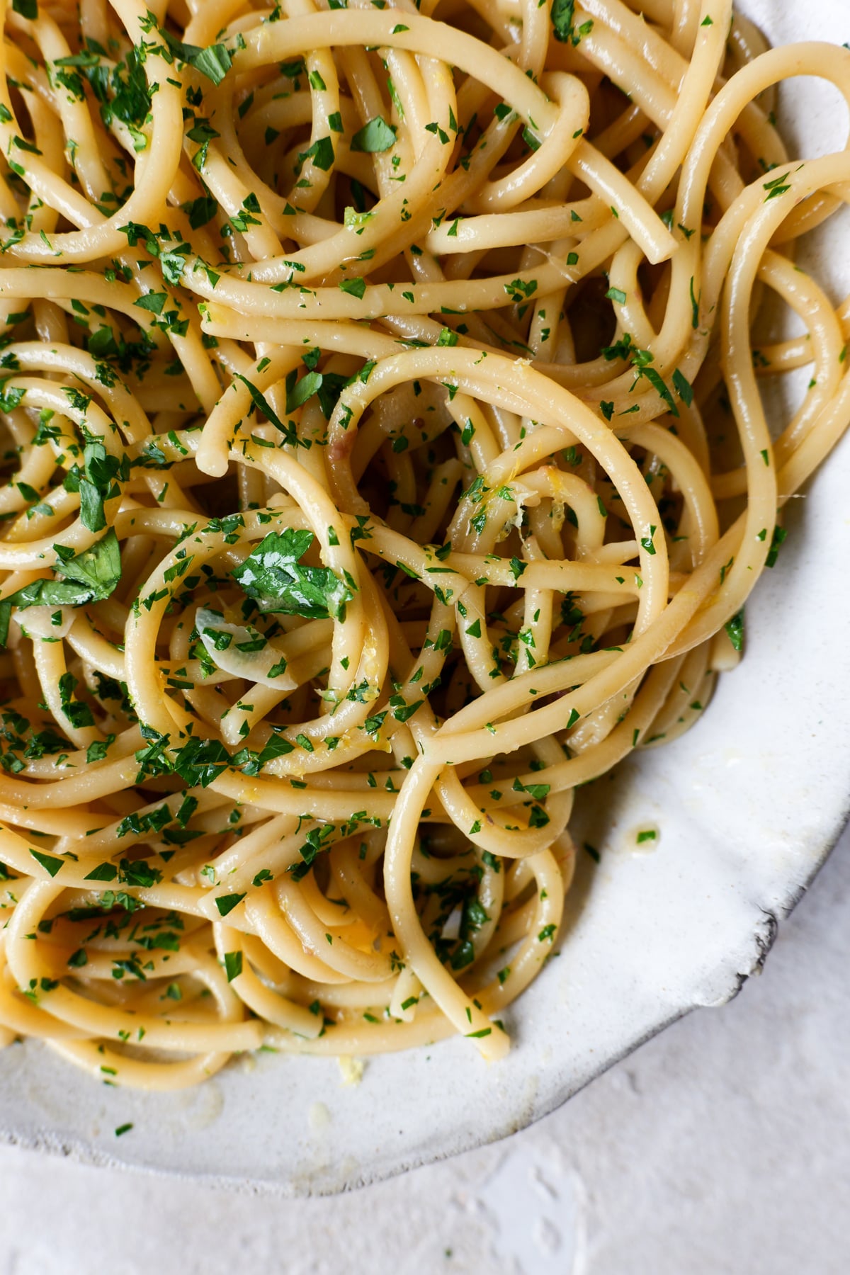 Anchovy butter pasta sits in large white bowl with fresh parsley sprinkled over the top.