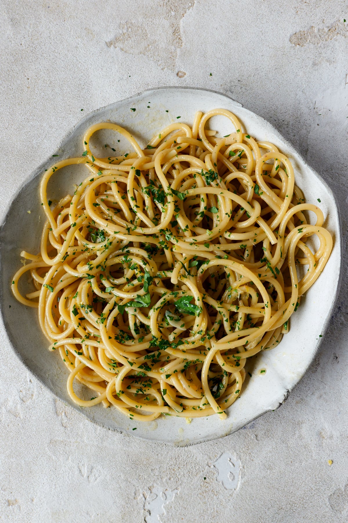 Anchovy butter pasta sits in large white bowl with fresh parsley sprinkled over the top.