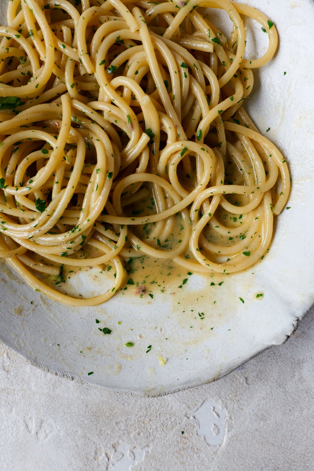 Anchovy butter pasta sits in large white bowl with fresh parsley sprinkled over the top.