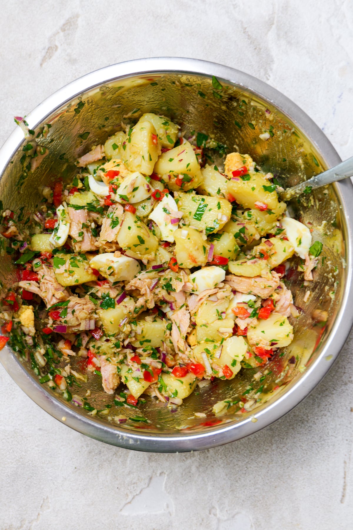 Stainless steel bowl shows everything for spanish potato salad all mixed together.