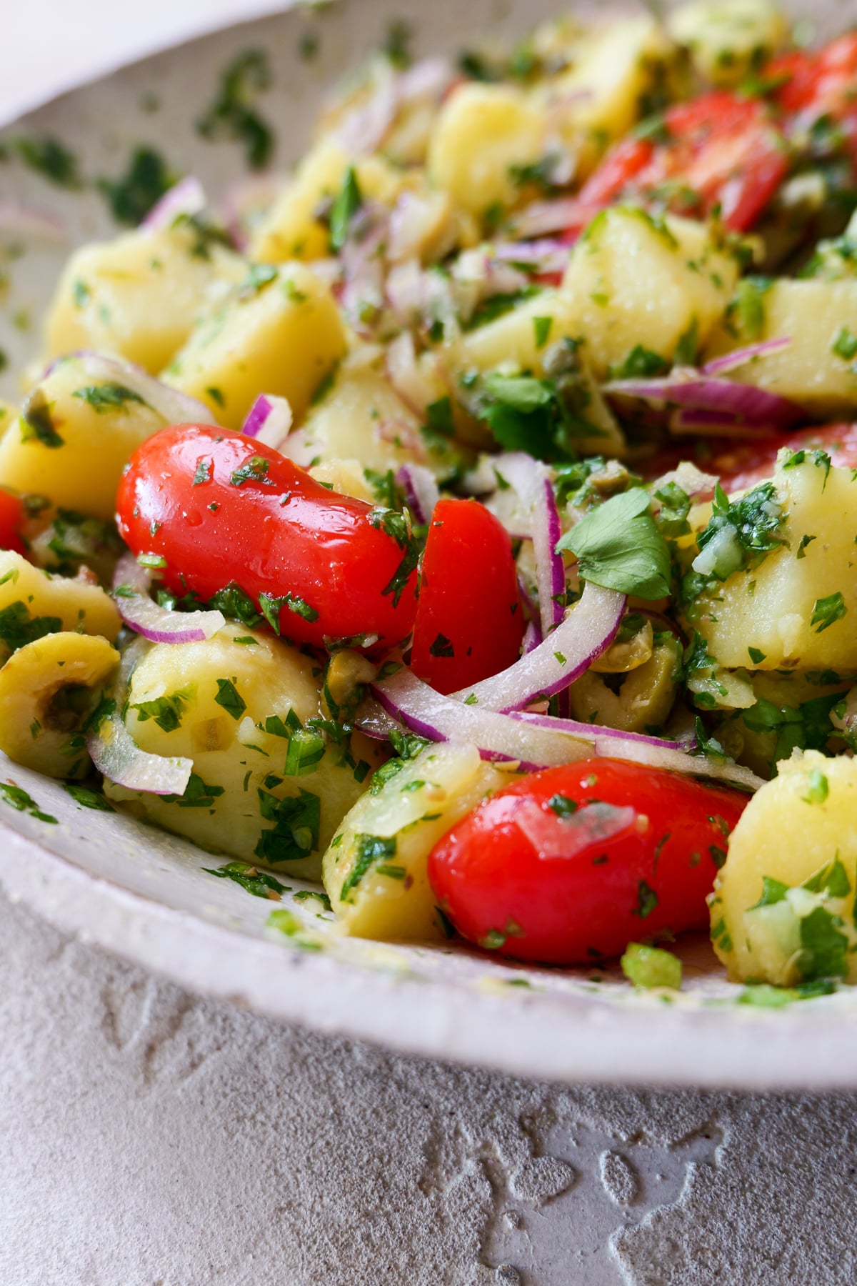 Italian potato salad in large white bowl with lots of fresh parsley sprinkled all over.