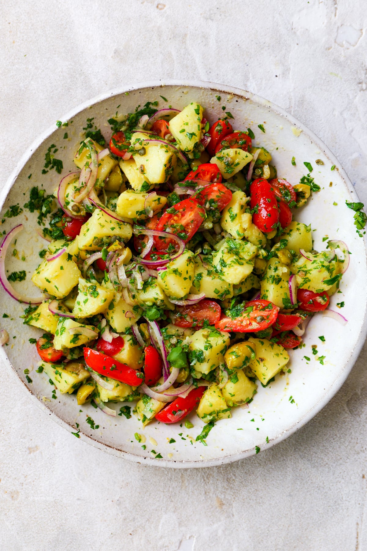 Italian potato salad in large white bowl with lots of fresh parsley sprinkled all over.