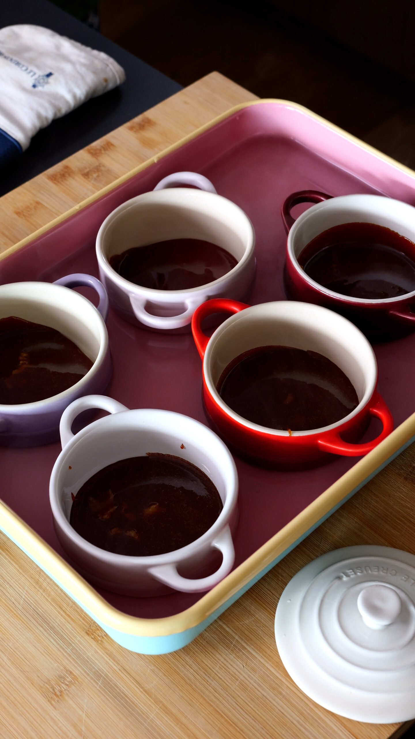 five ramekins are in large pink baking tray and have been filled with caramel