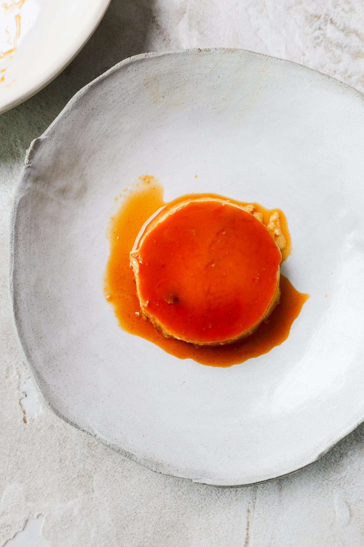 Spanish flan is in large white bowl with golden custard drizzled all over.
